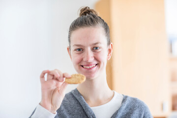Junge Frau mit blonden Haaren, Dutt, isst einen Keks in  der Wohnung
