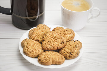 Close-up of freshly baked homemade cookies with additives. Shortbread cookies in the shape of a heart on a white saucer. Homemade cakes for breakfast and coffee in a white porcelain cup.