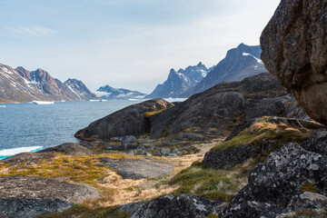 Rugged rocky landscape, with passenger ship moored in fjord and mountains with traces of snow in the background, Greenland