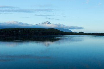 Fototapeta na wymiar Mountains with low clouds seen across a fjord during a late evening blue hour with mountains in soft focus, Hofn, Iceland