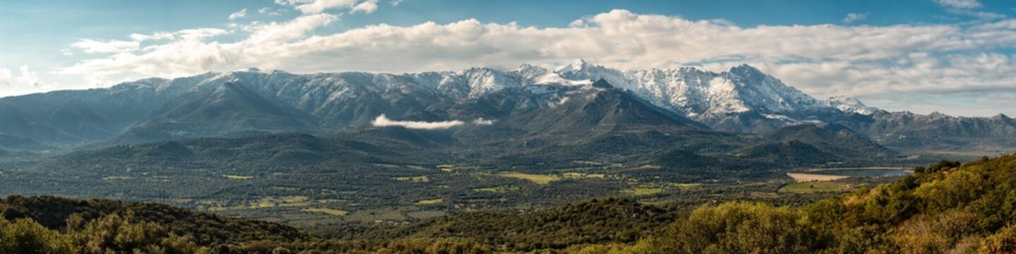 Panoramic view of the Regino valley and Lac de Codole in the Balagne region of Corsica with the snow capped peaks of Monte Padru, Monte San Parteo and Monte Grosso in the distance