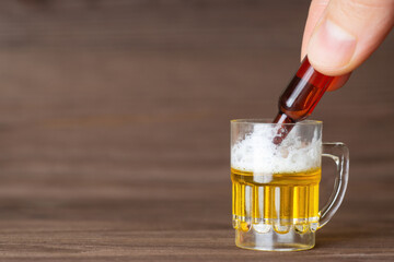Pouring beer from a tiny bottle into a small beer mug standing on a wooden table. Moderate alcohol...