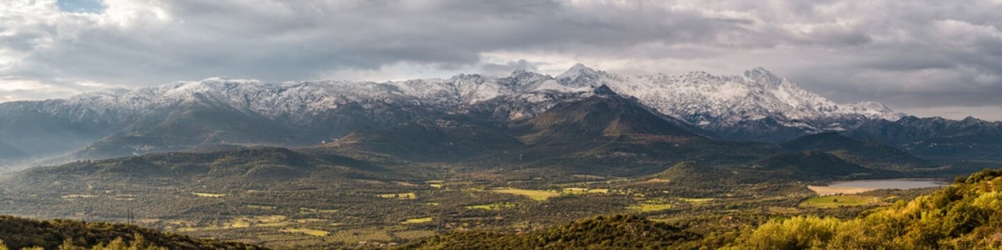 Panoramic view of the Regino valley and Lac de Codole in the Balagne region of Corsica with the snow capped peaks of Monte Padru, Monte San Parteo and Monte Grosso in the distance