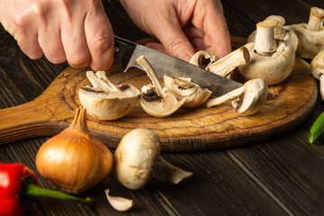 Slicing Agaricus mushrooms on a cutting board by the hands of a chef using a knife to prepare a...