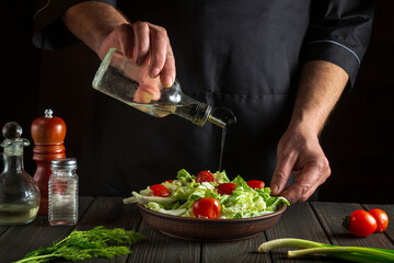 The chef pours oil into salad bowl in the kitchen. Cooking delicious and healthy food with a set of vitamins