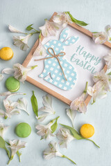 Delicate Easter background of white flowers, petals of colored macaroons and a frame with a bunny and the inscription "Happy Easter"