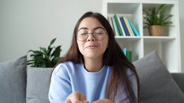 Happy funny caucasian teenager in glasses sitting on couch at home, gesticulation, looking at camera on laptop and talking cheerfully on video call with her girl friend, sister, mother. 4k footage
