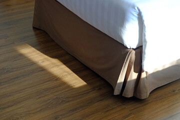 Bottom end of clean single bed on wood floor with sunlight in the morning