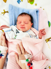 Woman holding her newborn baby with  peripheral venous catheter on her hand on hospital bed after birth.