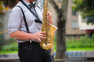 Man in blues or jazz suit, with black tie and black pants playing a saxophone in public in a public...