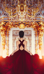 A young girl in a marsala red haute couture feather dress standing with her back in a luxurious...
