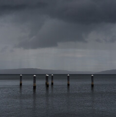Abandoned wooden pilings with white caps stand tall in Puget Sound on a stormy, rainy, grey day.