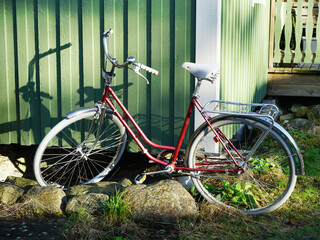 Red women's bicycle leaning against green cottage.