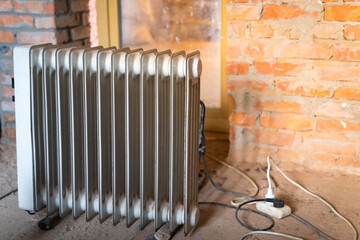 Old oil electric heater on the background of brick walls at a construction site. Heating of...