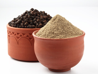 Indian spices Black Pepper powder in a terracotta bowl with pepper corns on white background
