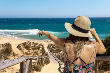 Young woman on her back with a hat pointing to the sea. Copy space. Selective focus.