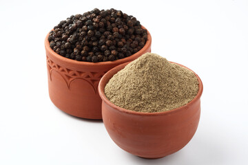 Indian spices Black Pepper powder in a terracotta bowl with pepper corns on white background
