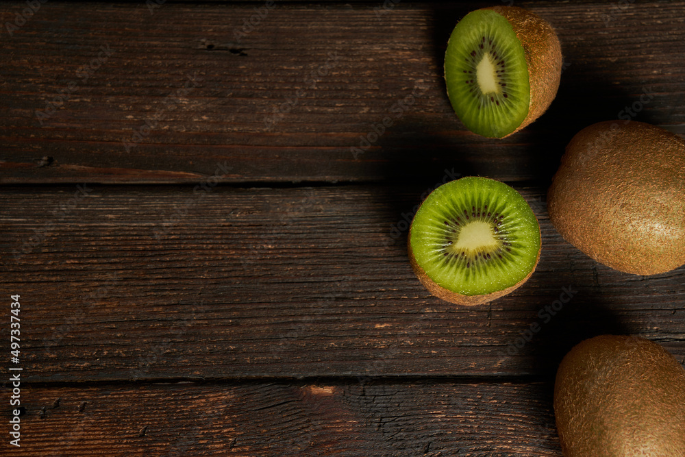 Wall mural One kiwi fruit cut in halves and two whole kiwi fruit isolated on wooden table and background. Copy space. Top view.