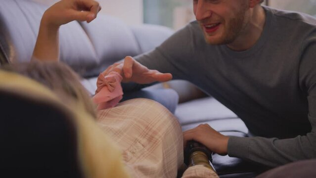 Man putting baby shoes on stomach of pregnant partner with prosthetic arm at home - shot in slow motion