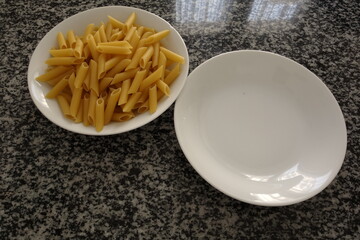 A plate of uncooked pasta and an empty plate on the table