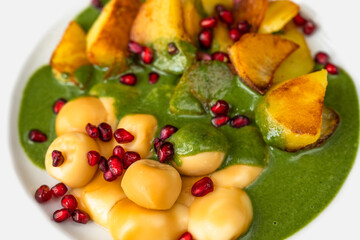 Smoked cheese balls, fried potato, spinach sauce and pomegranate seed, closeup.