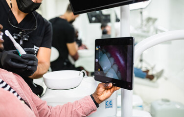 Dentist with face protective mask checking patient's teeth using wireless WiFi dental camera.