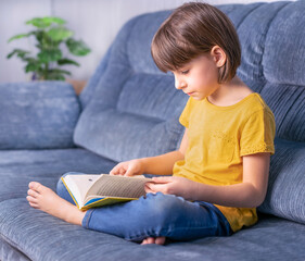 Little girl reading a book on the sofa