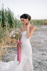 Summer portrait of a beautiful bride model at sunset in a wedding dress on the estuary