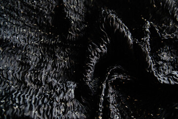 Crumpled black fabric lies in folds and drapery. Textile texture