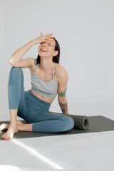 a beautiful girl sits on a rug in a blue-color sportswear. Girl covers her face with her hands