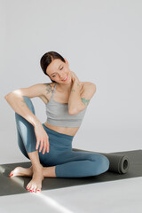 a beautiful girl sits on a mat in a blue-color sportswear. Girl massaging her neck