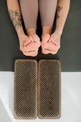The girl is sitting on a yoga mat. close-up feet hugging hands, stretching next to nailboard