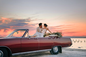 Beautiful couple at sunset on a summer wedding day. Romantic couple in love near their convertible....