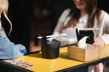 Two beautiful blonde and brunette girls order takeaway chinese food. Young woman outdoors speaking. Spring sunny day