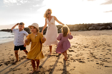 Happy beautiful family relaxing and dancing at the sunset beach in summer. Smiling mother with her two little daughters and one son having fun on vacations.