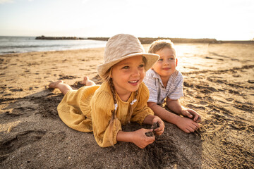 Lovely little kids playing at the beach. Cute boy and girl have fun together, lying on the sand and...