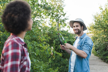 cheerful gardener cutting bushes near blurred african american woman.