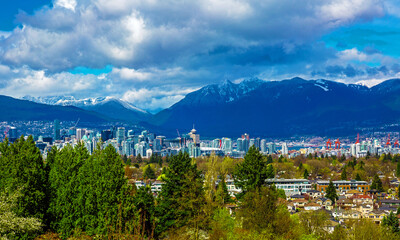 Aerial view of downtown of Vancouver and seaport  with the Rocky Mountains mountain range and stormy sky in the background and cityscape with green trees in the foreground