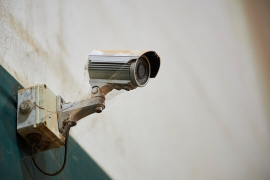 old surveillance camera. CCTV security camera. Security cameras on wall. White worn out old surveillance camera with peeling paint and connected to black cable.