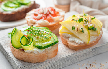 Crostini with soft cheese, cucumber, dill, apples, jam and nuts on a light background.