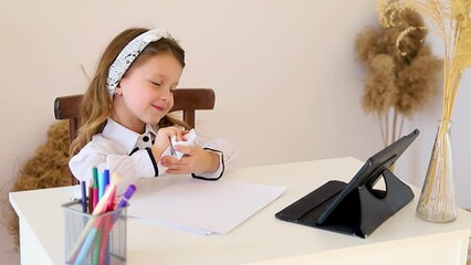Back to school. Happy little schoolgirl sitting at her Desk. The girl does her homework using a tablet computer. online education. - Powered by Adobe