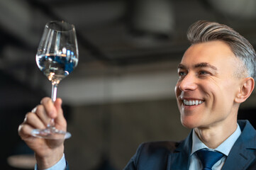 An elegant man in a suit with a glass of wine in hands