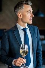 An elegant man in a suit with a glass of wine in hands