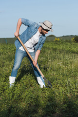full length view of farmer in brim hat and denim clothes digging in field.