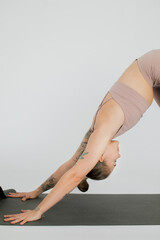 a young girl practices yoga downward dog pose on a yoga mat in a bright studio, close up shot