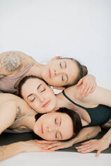 Obraz na płótnie Canvas three beautiful women closed their eyes, bowed their heads over each other, hugging each other. girls rest after yoga practice and meditate in a women's circle on a white background