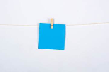 Post it azul colgado con pinza sobre fondo blanco para concepto ejercicio, recordatorio o mensaje.