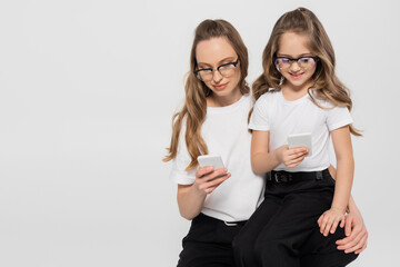 woman and child in eyeglasses using smartphones isolated on grey.