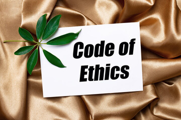 On beautifully curved golden silk lies a shefflera sheet and a white card with the text CODE OF...