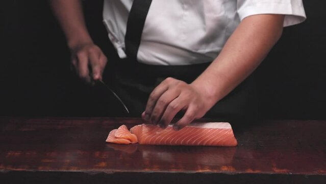 Chef's hand holding fresh piece of salmon.Closeup of chef hands preparing japanese food. Japanese chef making sushi at restaurant.Chef making traditional japanese sushi on wood board.